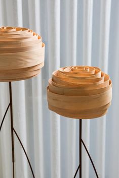 two wooden lamps sitting next to each other on top of metal stands with white curtains in the background