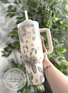 a person holding up a cup with a lid and handle in front of a plant