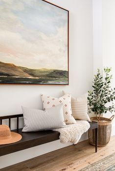 a painting hangs above a bench with pillows and a hat on it's head