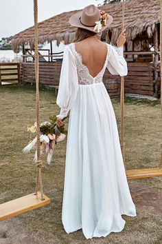 a woman in a white dress and hat on a swing with her back to the camera