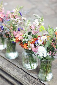 four glass vases filled with colorful flowers on top of a wooden table next to each other