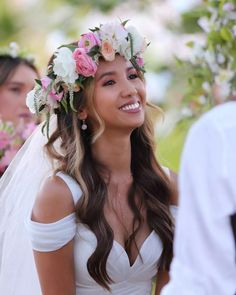 a woman in a wedding dress smiles as she stands next to another woman with flowers in her hair