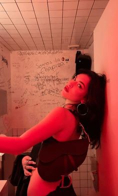 a woman standing in a bathroom next to a wall with writing on it and wearing headphones