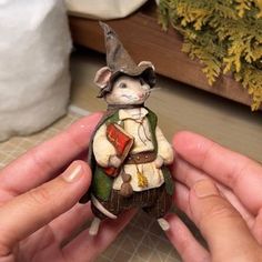 a hand holding a small figurine of a mouse wearing a hat and coat