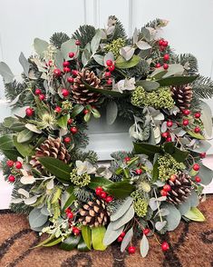 a wreath with pine cones, holly and red berries on the front door sill