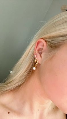 a woman with blonde hair wearing a pair of gold ear climbrs and pearl earrings