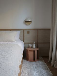 a white bed sitting in a bedroom next to a wooden table with two vases on it