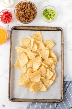 tortilla chips on a baking sheet with salsa and dressings in the background