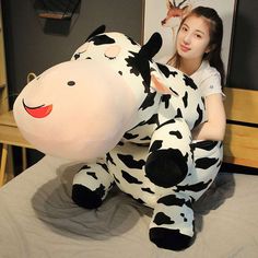 a woman sitting on top of a bed next to a large cow stuffed animal in the shape of a cow