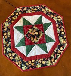 a red and green quilted table topper on a wooden surface with flowers in the center