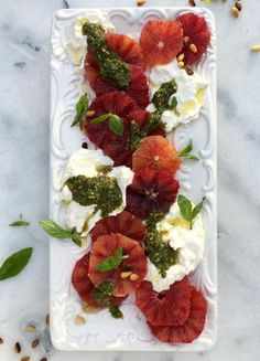 a white plate topped with fruit covered in cream and green toppings on top of a marble table