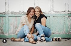 two young women sitting on the ground posing for a photo with their arms around each other