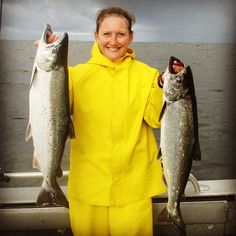 a woman in yellow is holding two fish and smiling at the camera while standing on a boat