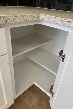 an empty white kitchen cupboard with marble counter tops and cabinets in the corner that are open