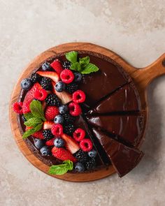 a chocolate cake with berries, raspberries and mint leaves on top is cut into slices