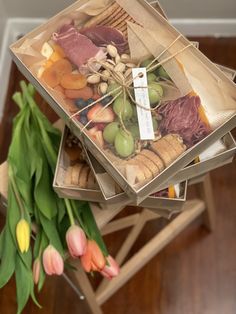 three boxes filled with different types of food on top of a wooden table next to tulips