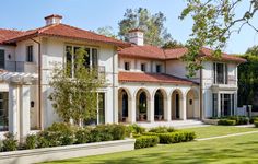 a large white house with lots of windows and red tile on the roof is surrounded by greenery