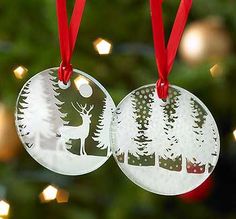 two christmas ornament hanging from a tree with lights in the background and red ribbon