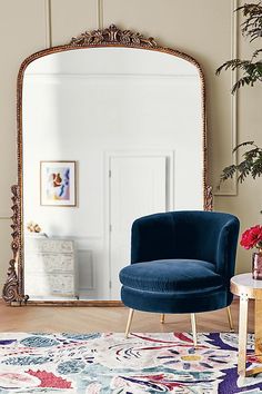 a blue chair sitting in front of a mirror on top of a wooden floor next to a table