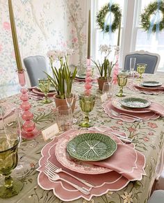 the table is set with pink and green plates, place settings, and greenery