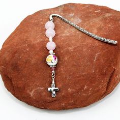 a pink beaded bracelet with a silver cross charm on top of a red rock