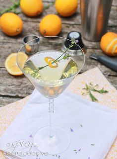 a glass filled with liquid sitting on top of a wooden table next to oranges