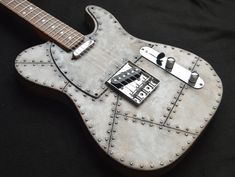 an electric guitar sitting on top of a black cloth covered floor with metal rivets