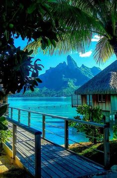 a wooden walkway leading to a beach with mountains in the background and blue water on both sides