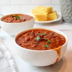 two bowls of chili and cornbreads on a white counter with a towel next to them