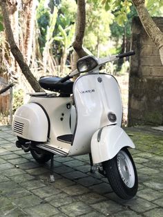 a white scooter is parked in front of some trees