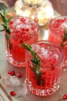 three glasses filled with red liquid and garnished with rosemary sprigs on a tray