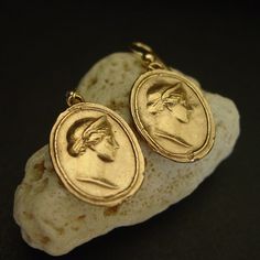 two gold earrings with an image of a man's head on them sitting on top of a rock