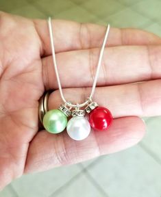 a person holding three different colored pearls in their hand, one is silver and the other is red