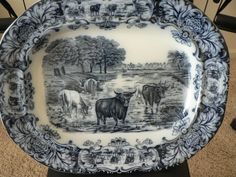 an antique blue and white platter with cows on the side, in front of a table cloth