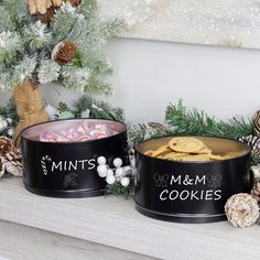 two tins filled with cookies sitting on top of a mantle next to pine cones