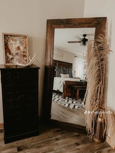 a mirror sitting on top of a wooden floor next to a black dresser and lamp