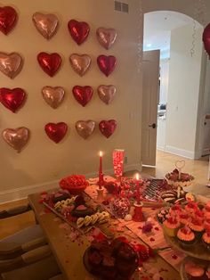 a table topped with lots of cupcakes covered in pink frosting and heart shaped balloons