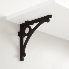 an iron shelf bracket on the corner of a white wall with black brackets hanging from it's sides