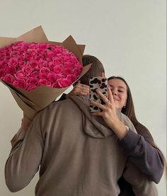 a woman taking a photo with her cell phone while holding a bouquet of pink roses