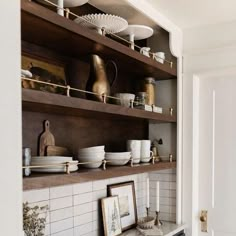 a kitchen shelf filled with white dishes and gold vases on top of wooden shelves