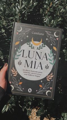 the book lunaa mia is being held up by someone's hand in front of some plants