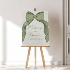 a welcome sign with a green bow on it in front of a white wall and wooden easel