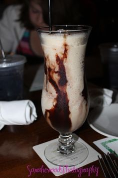 a glass filled with liquid sitting on top of a wooden table next to a fork