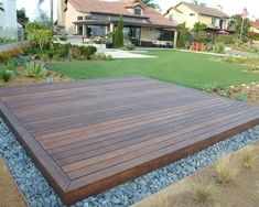 a large wooden deck in front of a house with grass and rocks on the ground