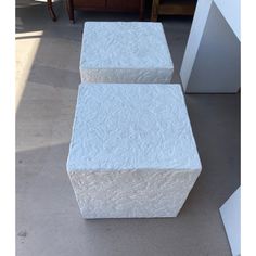 two white stools sitting on top of a cement floor next to a wooden table