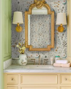 a bathroom vanity with a gold framed mirror above it and flowers on the wall behind it