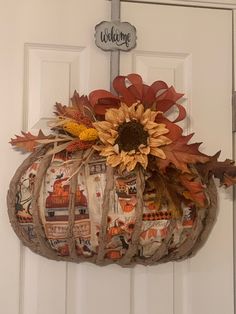 a decorated pumpkin hanging on the front door with a welcome sign above it and sunflowers