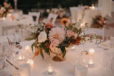 an arrangement of flowers and candles on a table at a wedding reception with white linens