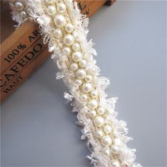 a white lace with pearls is shown on the edge of a piece of fabric, next to a ruler