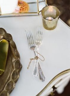 a white table topped with silverware next to a small mirror and candle holder on top of it